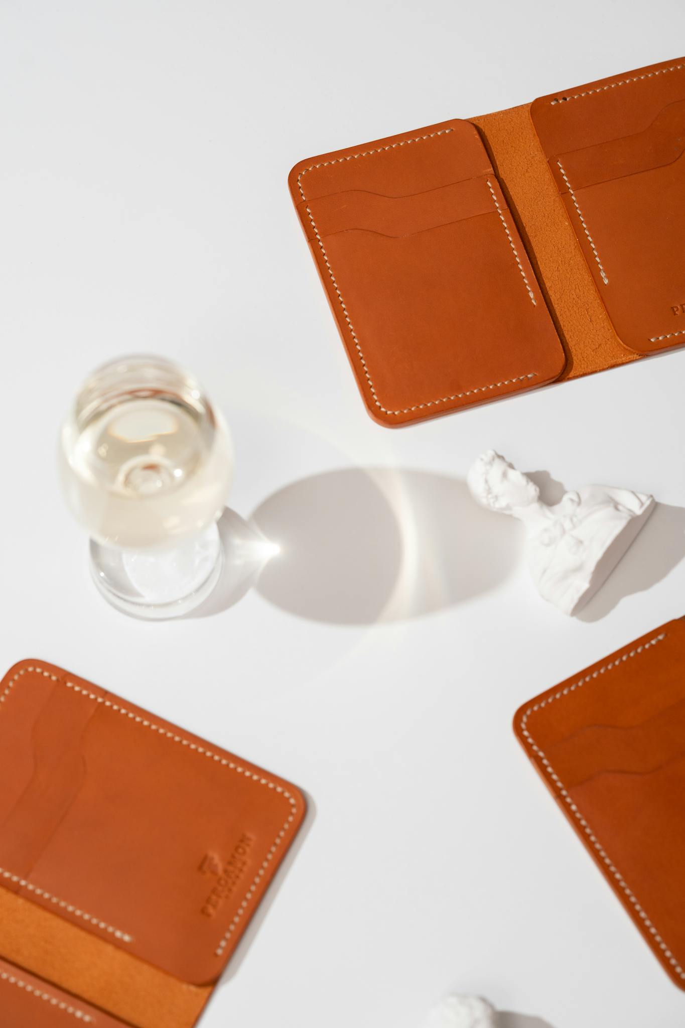 Elegant composition of leather wallets with wine glass and sculpture on a white background.