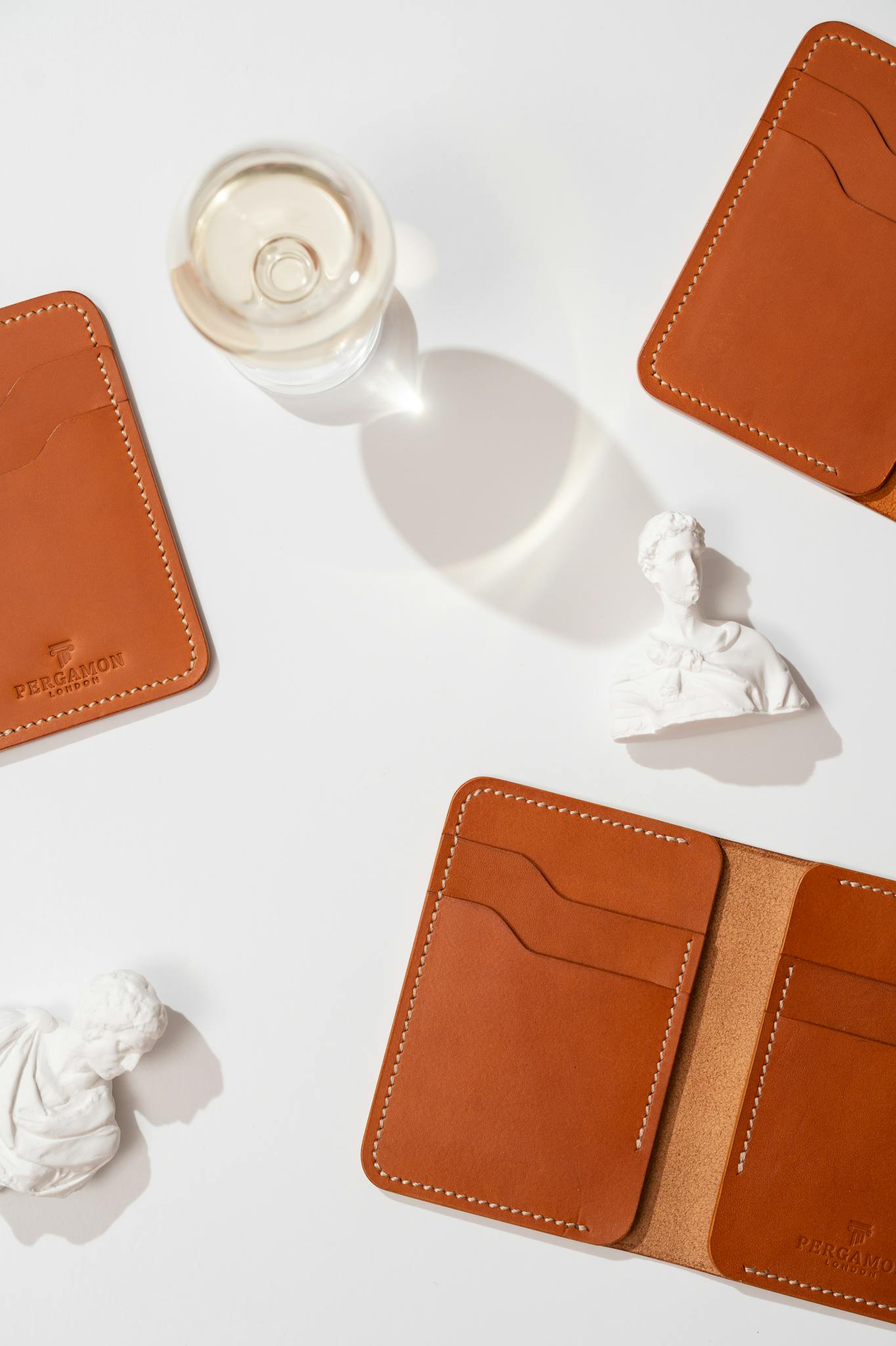 Flat lay of brown leather wallets with white classical sculptures on a white background.