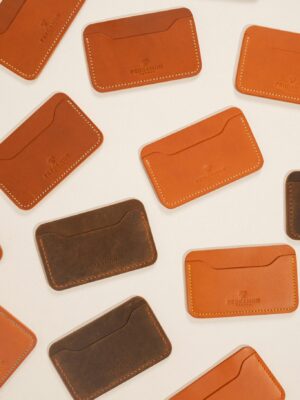 Flat lay of stylish brown and orange leather card holders on cream background.