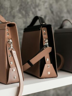 Luxury leather handbags displayed on a white shelf, showcasing minimalistic design and various colors.